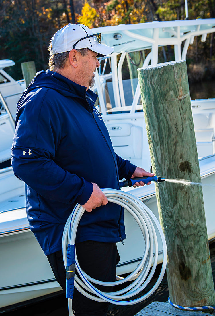 Man spraying a white and blue hose near a boat