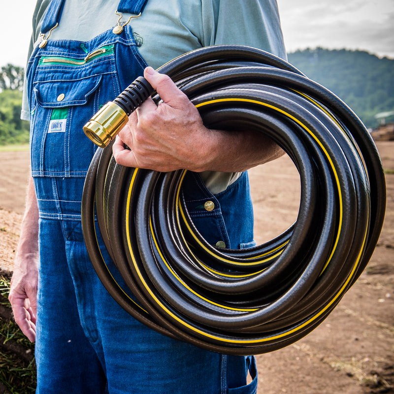 A farmer holding a black and yellow hose around his forearm