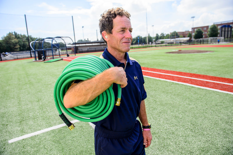Man on a sports field holding a coiled green hose