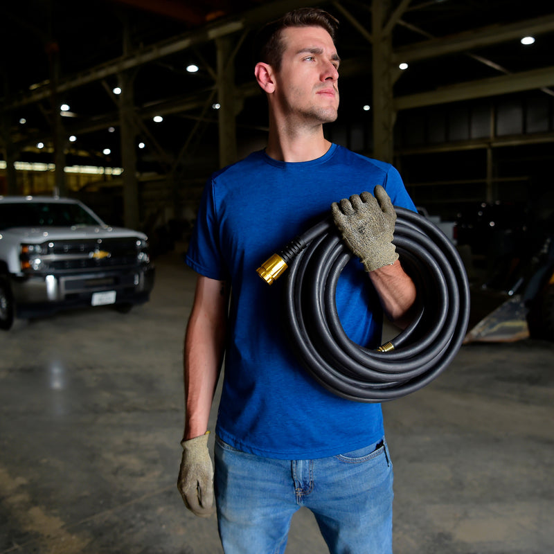 Man holding a coiled up black rubber hose in a garage