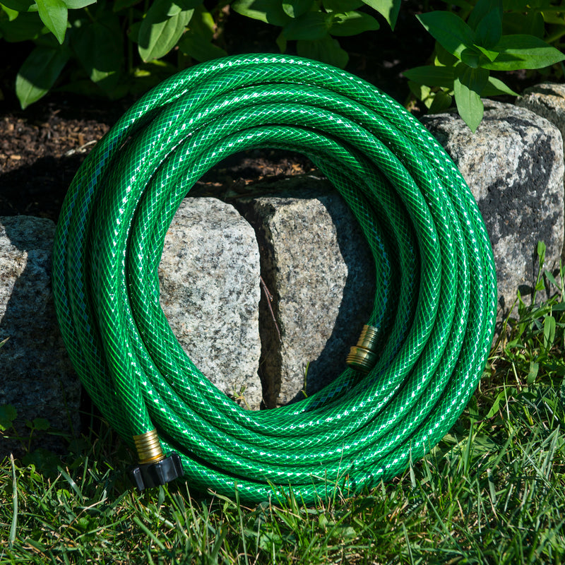 Coiled green hose leaning against a garden bed